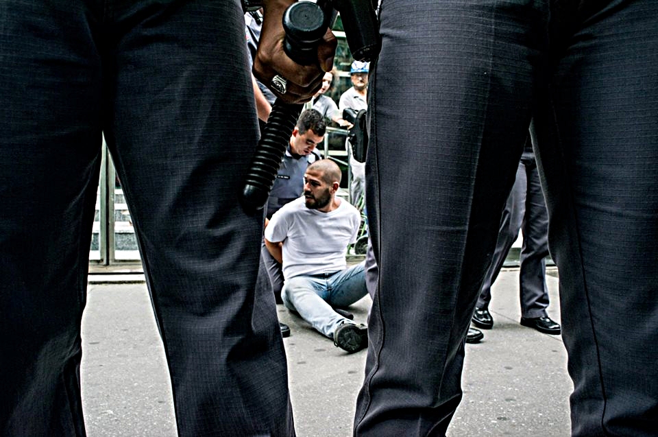 Caio Castor rendido e algemado, espera ser levado para uma delegacia em um verdadeiro desrespeito aos direitos humanos. Foto: Vinicius Gomes.